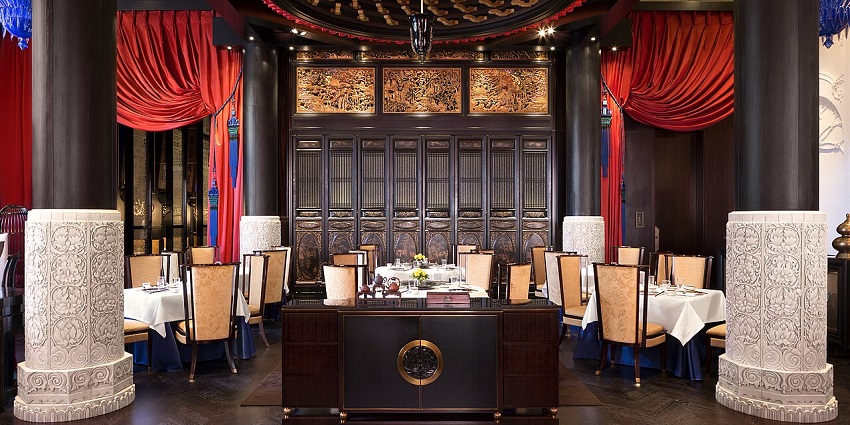 A formal dining room with red curtains, white tablecloths, and ornate wall carvings.
