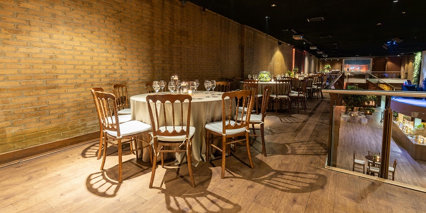 Elegant dining space with round tables, wooden chairs, brick walls, and warm lighting
