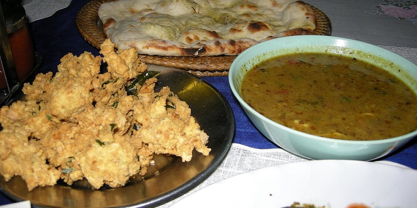 A plate of pakoras is served with a bowl of dal and naan in the background at one of the pure veg restaurants in Neil Island.
