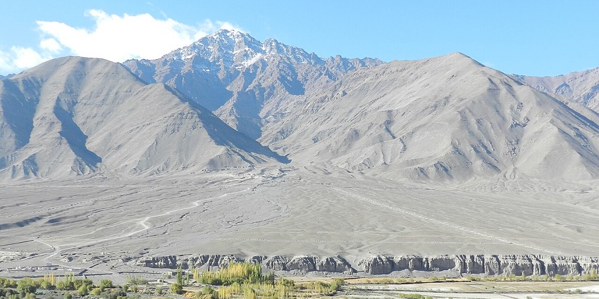 A wide landscape of a river and trees flowing through a valley with large gray mountains.