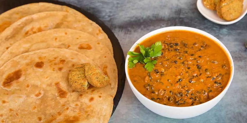 A bowl of creamy lentil curry next to a stack of delicious flatbread and small fritters.