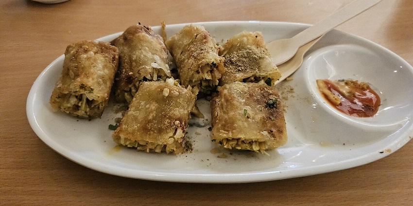 A plate of spring rolls with red sauce is served with a cup of tea at a restaurant.