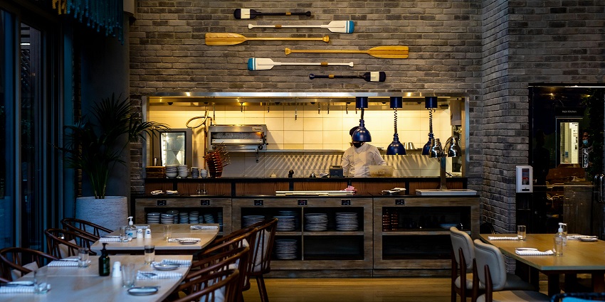 Restaurant interior featuring open cooking station, rustic décor, and neatly arranged seating
