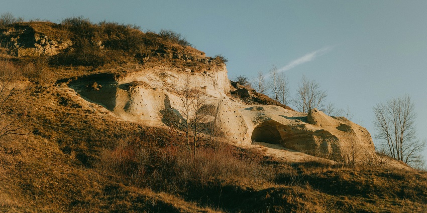 Natural rock archway at Sidlaphadi Caves surrounded by dry grass and open sky.
