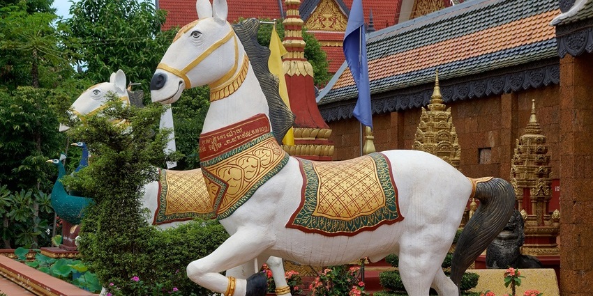 A statue of a horse stands in front of the ornate and colourful Wat Preah Prom Rath Buddhist temple.