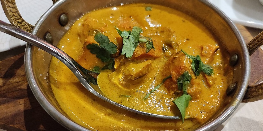 A bowl of hot Indian curry, topped with fresh cilantro, served with a spoon
