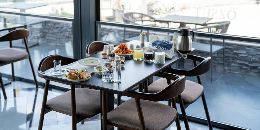 Restaurant table by glass windows set with soup, bread rolls, drinks, and a coffee pot.