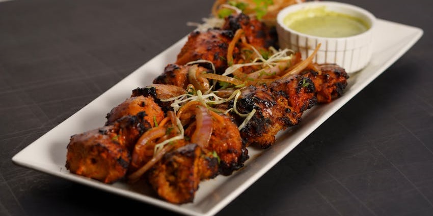 Grilled chicken tikka served on a sizzling platter alongside a dipping sauce.