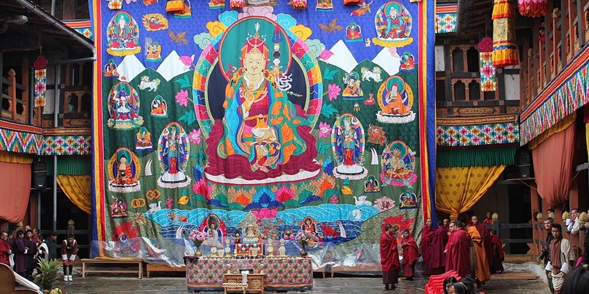 Monks dressed in red robes stand near a Buddhist deity during the Tsechu festival in Bhutan.