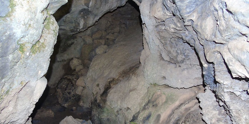 Close-up of rocky walls and floor of narrow cave with dark opening, caves in Uttarakhand.
