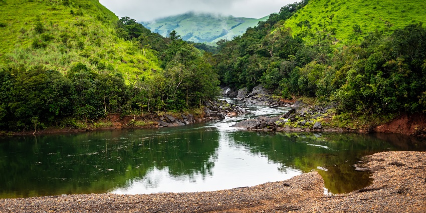 Tadiandamol Trek with mountain gap, river flowing, and lush green forests around.