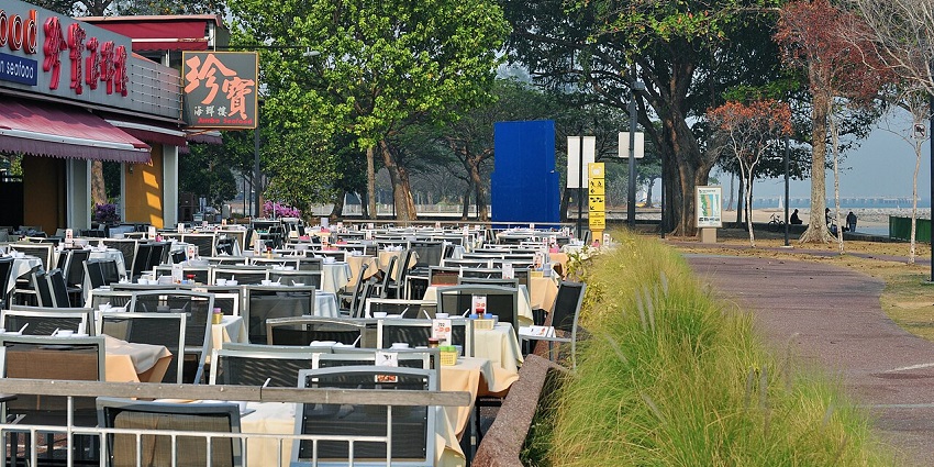 Outdoor dining setup at a seafood restaurant in Singapore near lush green trees.
