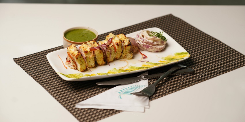 A plate with grilled meat, a small bowl of sauce, and a side of sliced onions served at Tandoor Restaurant.
