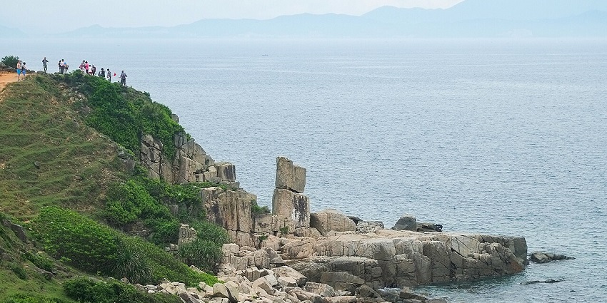 Tap Mun Island with people standing on the cliff covered in greenery and rocks lining the shore.