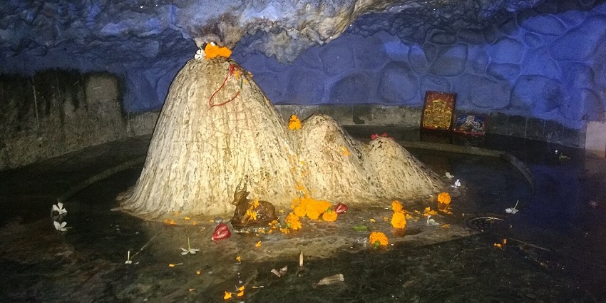 Small shrine in cave with white rock mounds and flowers, one of the caves in Uttarakhand.
