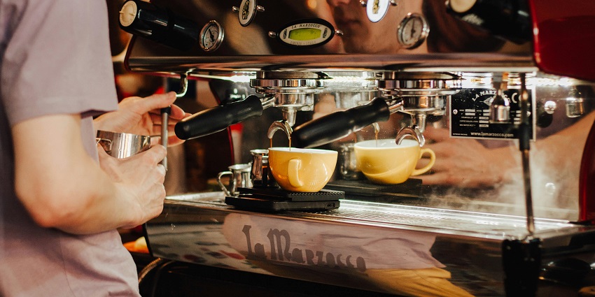 A barista using an espresso machine to brew coffee into yellow cups at a busy cafe counter, one of the cafes in Port Blair.