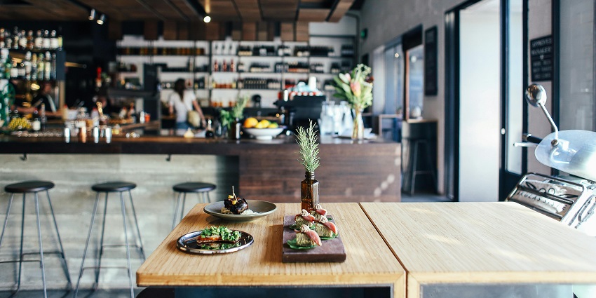 Modern café interior with wooden décor, bar counter, and plated dishes on a table.
