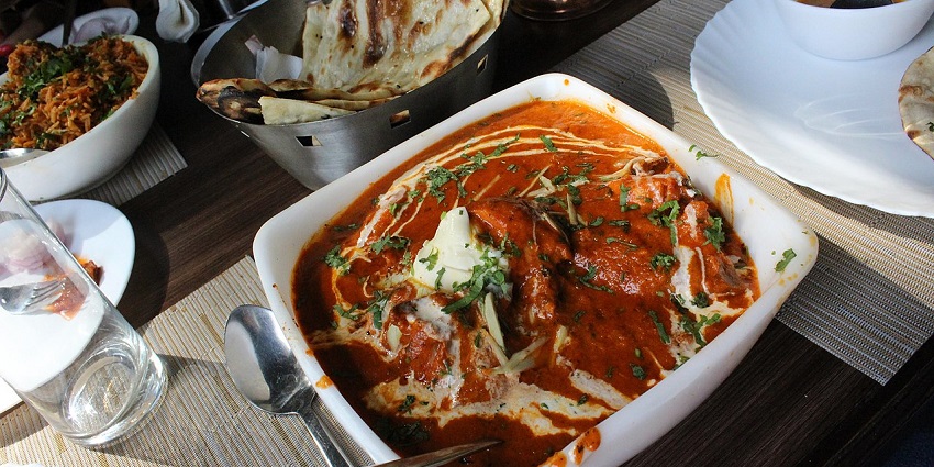 A close-up shot of a rich, creamy butter chicken dish served in a bowl with naan bread in one of the restaurants in City Centre Siliguri.
