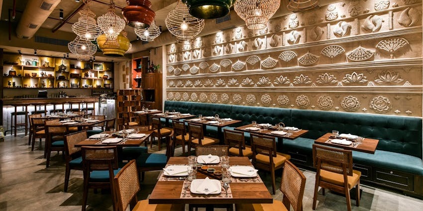 The Kitchen Restaurant with carved wall art, hanging lamps, and neatly set wooden tables.