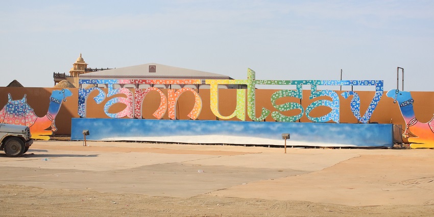 Rann Utsav sign on display with colourful camel stands on both sides.

