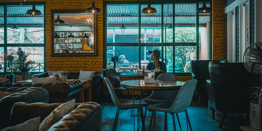 Cosy café with brick walls, chandeliers, leather sofas, and a man seated by the window
