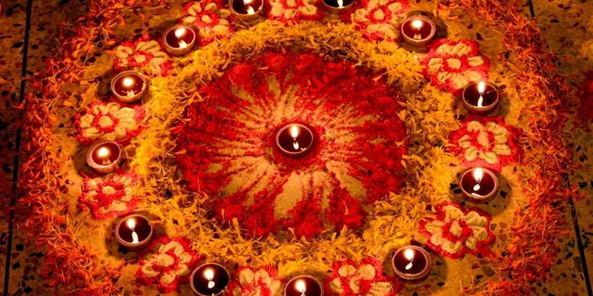 Colorful flower rangoli with a lit diya placed in the center and around, creating a festive vibe.
