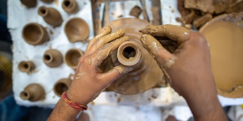 Potter's hands, covered in clay, crafting a beautiful vase on a wheel at pottery workshop.