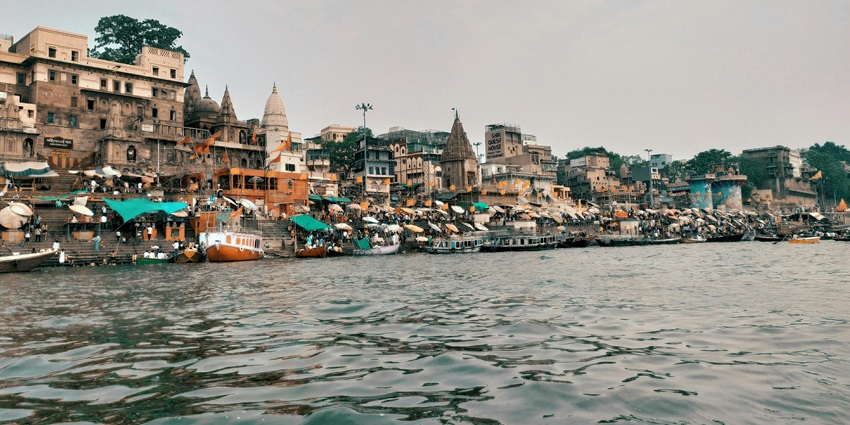 View of a bustling ghat along the river with boats and people during the day.