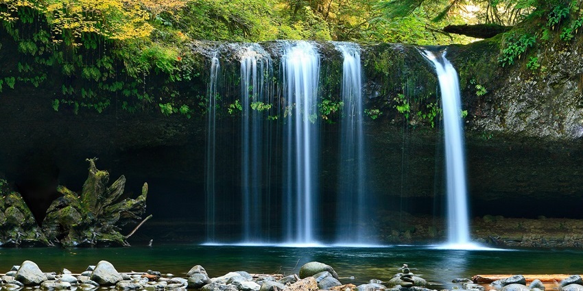 Thin waterfall streams dropping from a rocky ledge into a calm pool with pebbles, one of the best waterfalls in Andaman.
