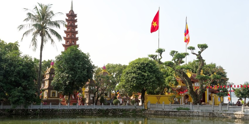 Trấn Quốc Pagoda in Hanoi, with a tall red stupa, trees, and reflection in West Lake, one of the temples in Vietnam.