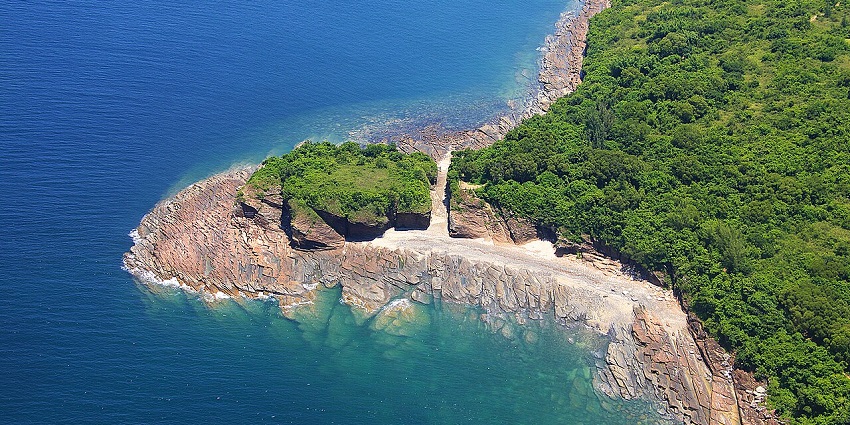 Tung Ping Chau Island from above with rocky cliff covered in greenery and lining the shore.