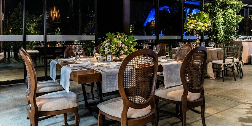 Dining table with floral centrepiece, wooden chairs, and large windows overlooking greenery.
