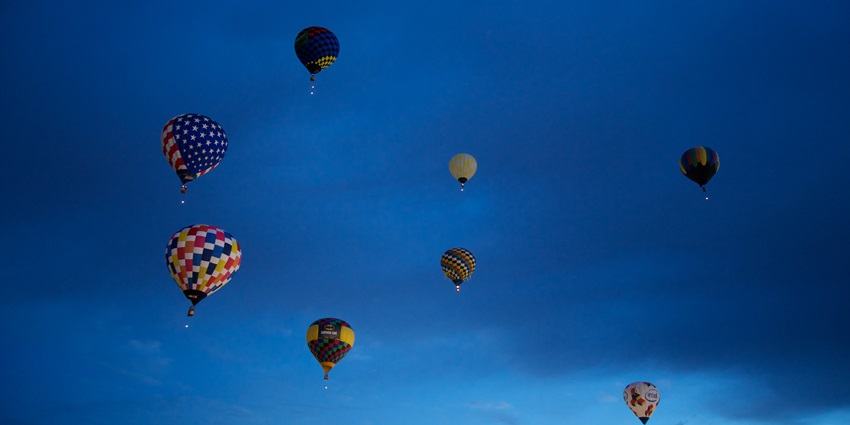 A few hot air balloons hovering against the dark blue sky for the dawn patrol early morning.