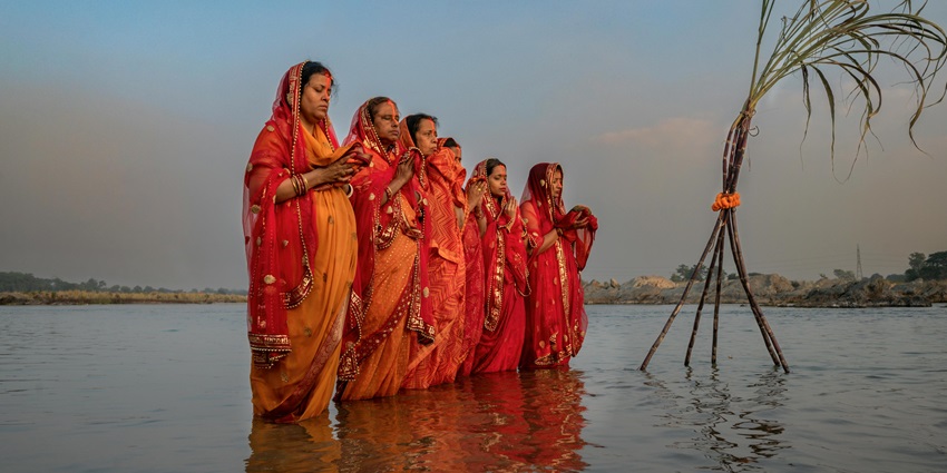 Several women are offering prayers during the sunrise while standing on a large body of water.