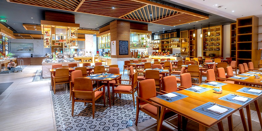 Spacious modern restaurant with wooden furniture, patterned flooring, and buffet counters, one of the restaurants in Guwahati.
