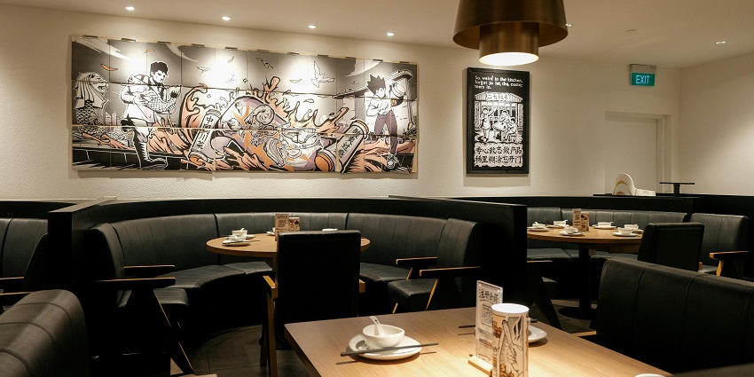 Restaurant with black booths, round wooden tables, and comic-style artwork on the wall.