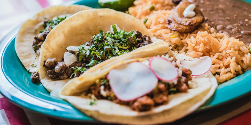 A plate of Mexican food served with taco, rice, and gravy on a dining table.