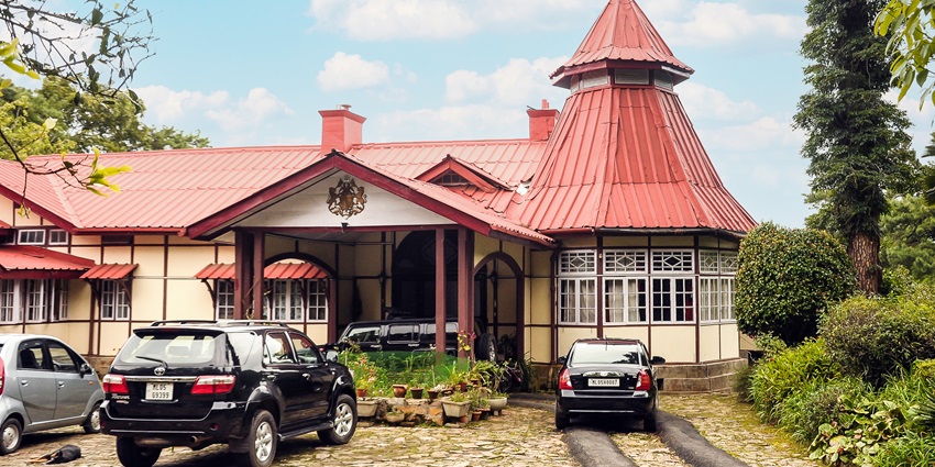 Tripura castle stay in Shillong with multiple vehicles parked in front of the building and greenery.