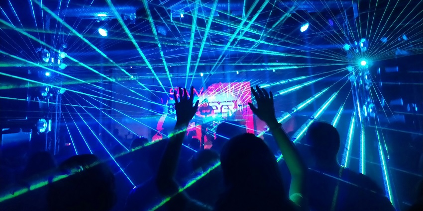 Close-up, low-angle shot of hands of a DJ working on a mixing board with colourful lights.
