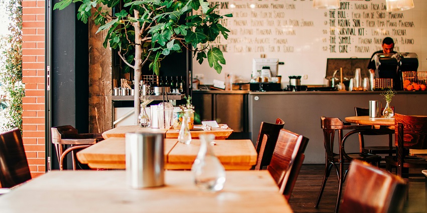 Cosy café with wooden tables, indoor tree, and a juice bar counter with handwritten menu, one of the best restaurants in Orchard.