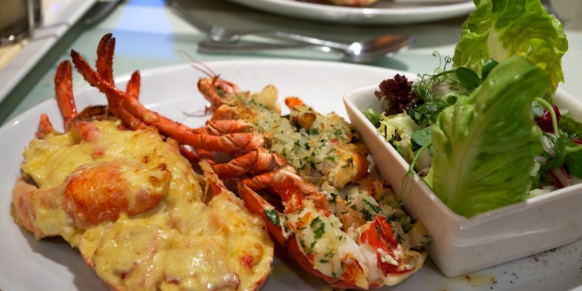 A platter with a lobster thermidor and a lobster covered with cheese, and a side salad.
