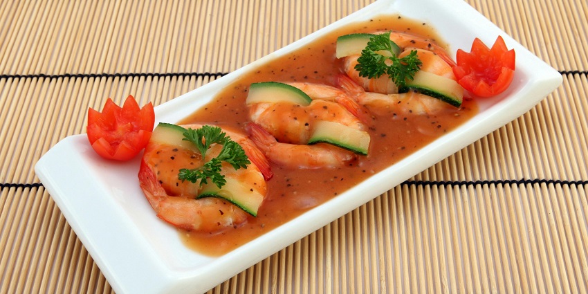 A wide, shallow bowl holds a plate of pasta with large shrimp and a green leaf garnish.
