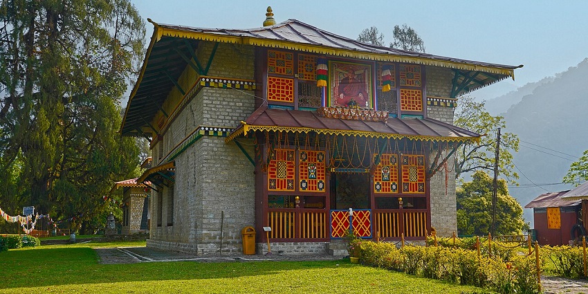 Dubdi monastery, decorated with colourful flags, stands on a green lawn alongside other buildings.
