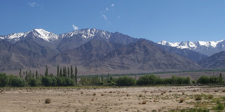 A wide shot of mountains with snow-capped peaks, a blue sky, and a grassy foreground.