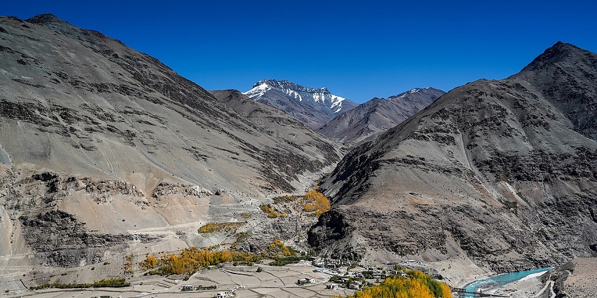 A picturesque mountain valley with a small village surrounded by golden trees and a river at Zanskar Valley Wildlife Santuary in Ladakh.
