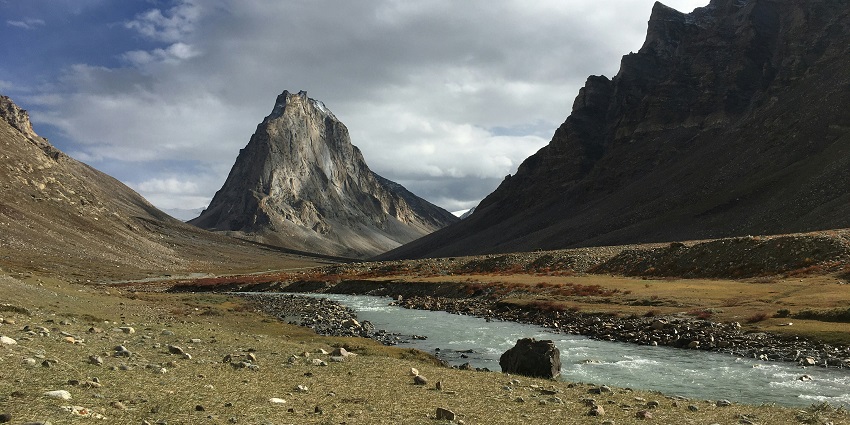A scenic mountain valley with a small village ringed by golden trees and a river.
