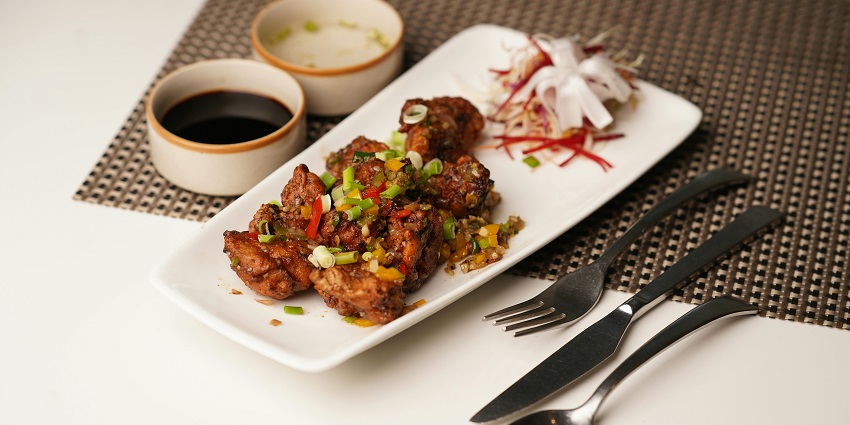 Plate of fried chicken pieces with peppers, spring onions, sauces, and salad garnish.