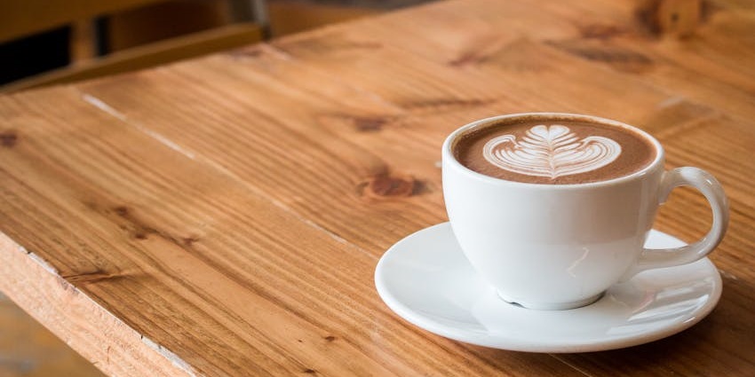 Cappuccino on a wooden rustic table with latte art on top served at By The Way Restaurant.