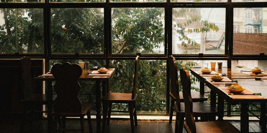 Wooden dining tables by windows with rooftop views, one of the restaurants in Aizawl.