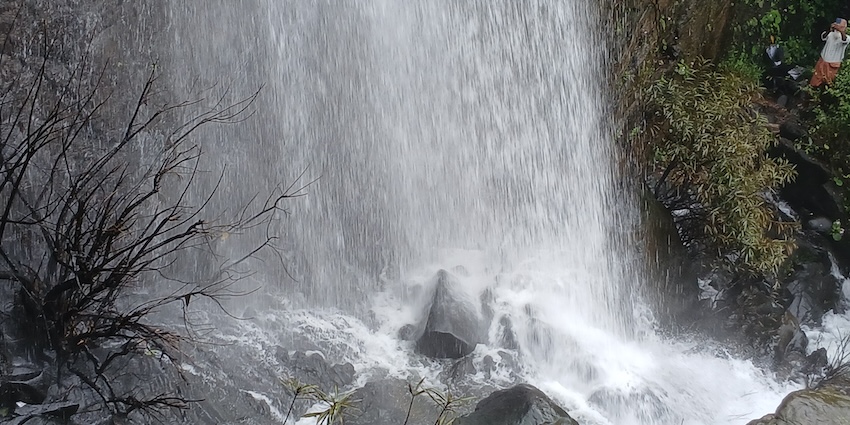 A thick curtain of whitewater falling steeply over dark rocks with a person watching.